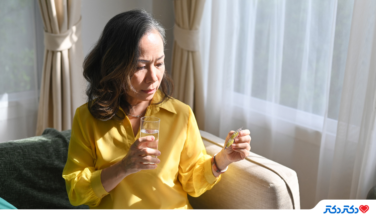خانمی میاسال نشسته بر روی مبل با یک لیوان آب و در حال خوردن قرص