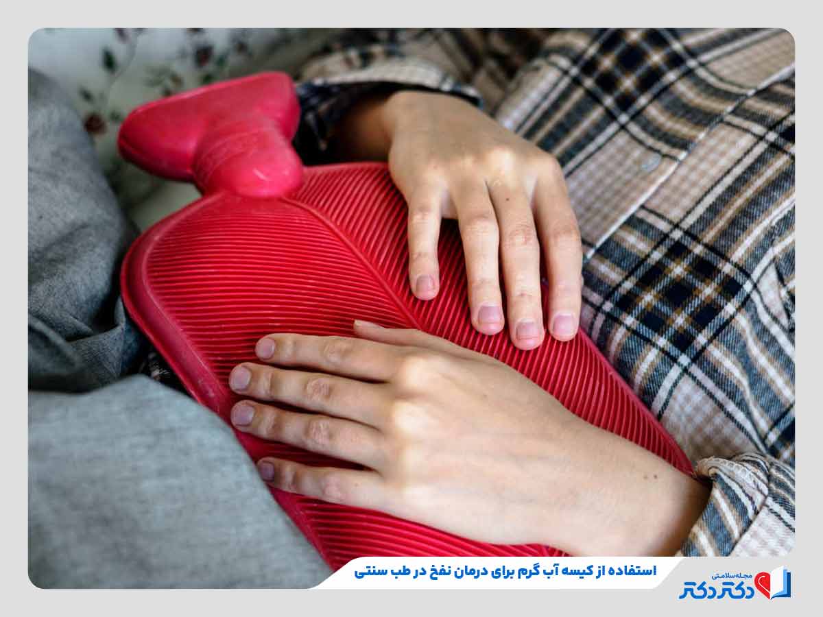 زن در حال استفاده از کمپرس آب گرم به عنوان درمان نفخ شکم با طب سنتی